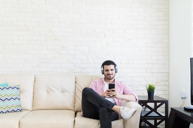 Joven vlogger con auriculares mientras usa el teléfono móvil en el sofá