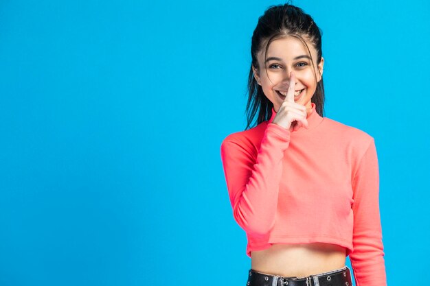 Jovencita alegre sonriendo y llevándose el dedo a la boca Foto de alta calidad