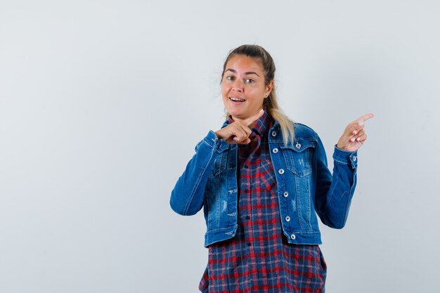 Jovencita apuntando a un lado en camisa, chaqueta y mirando confiado, vista frontal.