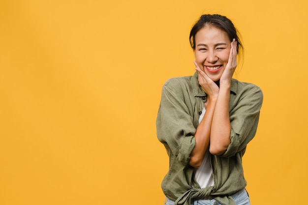 Jovencita asiática con expresión positiva, sonrisa amplia, vestida con ropa casual sobre pared amarilla. Feliz adorable mujer alegre se regocija con el éxito. Concepto de expresión facial.