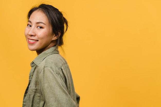 Jovencita asiática con expresión positiva, sonrisa amplia, vestida con ropa casual sobre pared amarilla. Feliz adorable mujer alegre se regocija con el éxito. Concepto de expresión facial.