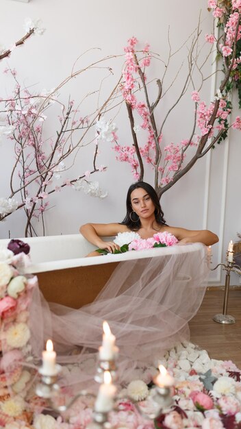 Jovencita caliente sentada en una bañera con flores y mirando a la cámara Foto de alta calidad