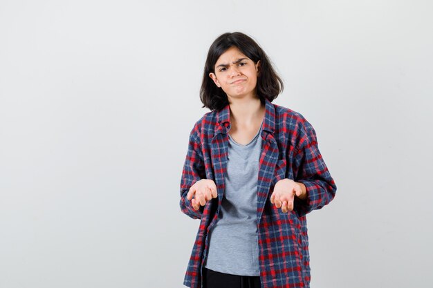 Jovencita en camisa a cuadros disgustada con una pregunta tonta y luciendo triste, vista frontal.