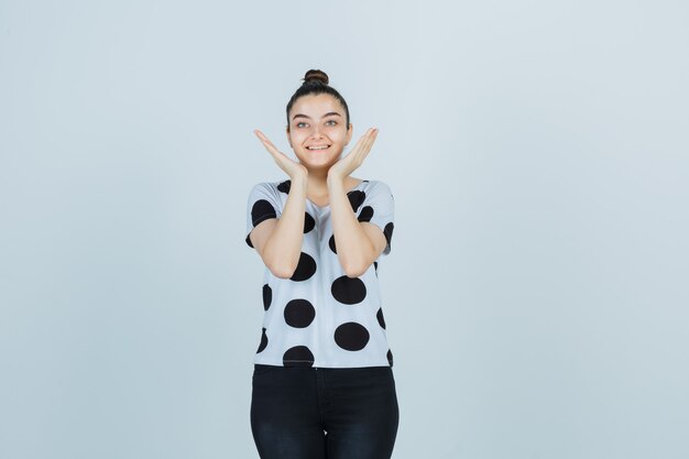 Foto gratuita jovencita en camiseta, jeans tomados de la mano cerca de las mejillas y luciendo linda vista frontal.