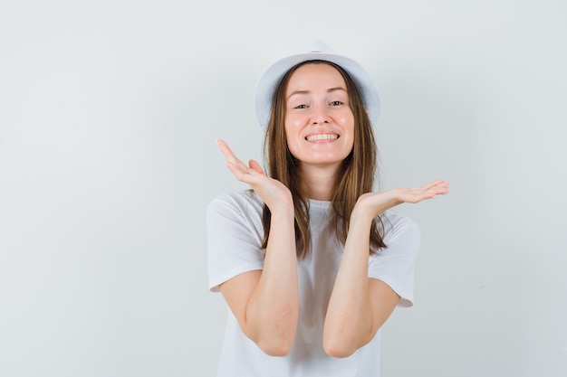 Jovencita cogidos de la mano cerca de la cara con sombrero de camiseta blanca y aspecto lindo