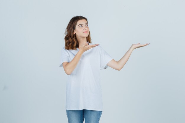 Jovencita dando la bienvenida en camiseta, jeans y luciendo bonita. vista frontal.