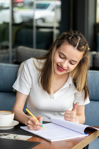 Jovencita escribiendo sus notas y gesticulando con el pulgar hacia arriba en el restaurante