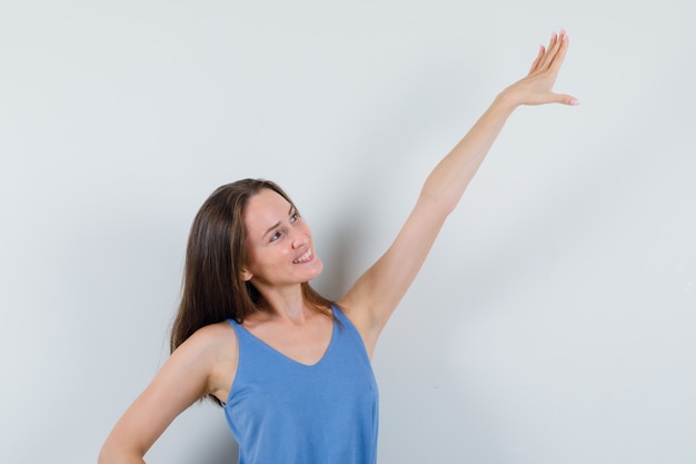 Jovencita estirando el brazo en camiseta, falda y mirando alegre, vista frontal.