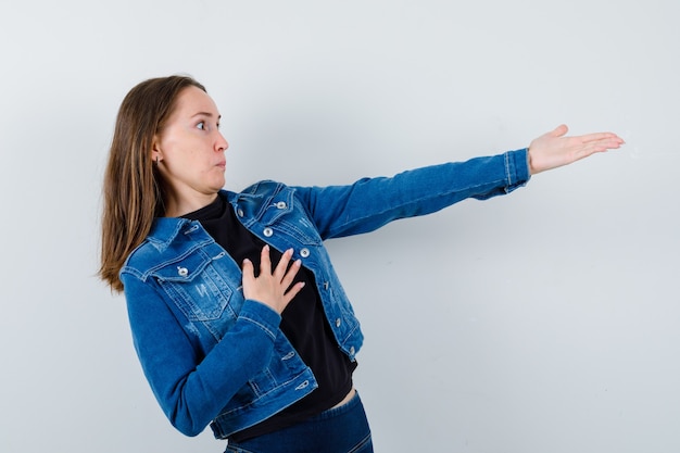 Foto gratuita jovencita estirando la mano para mostrar algo en blusa, chaqueta y mirando sorprendido. vista frontal.