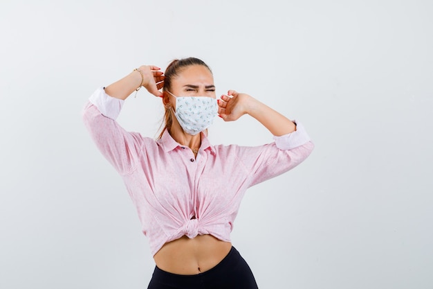 Jovencita estirando la parte superior del cuerpo en camisa, máscara y aspecto relajado. vista frontal.