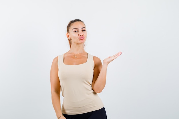 Jovencita extendiendo la palma hacia un lado, haciendo pucheros con los labios en la camiseta sin mangas y luciendo linda vista frontal.