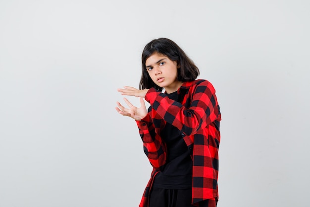 Jovencita fingiendo sostener algo en camisa casual y mirando pensativo, vista frontal.