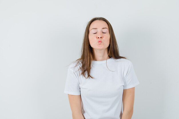 Jovencita haciendo pucheros con los labios en camiseta blanca y luciendo linda