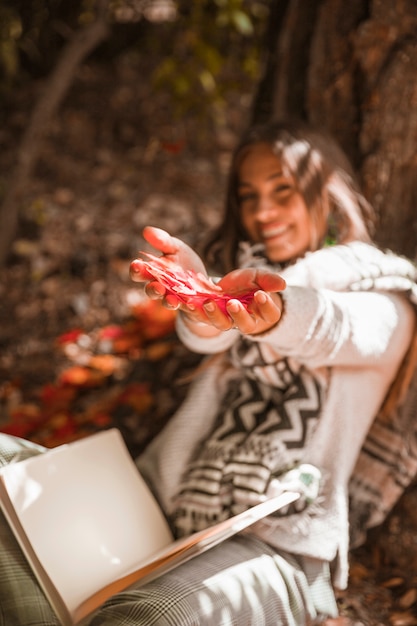 Foto gratuita jovencita con libro mostrando hojas de otoño