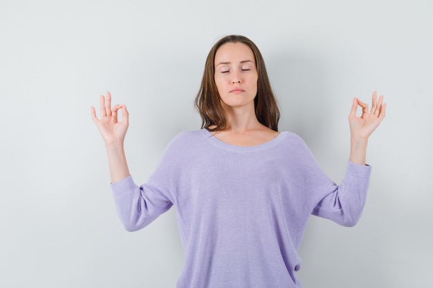 Jovencita mostrando gesto de meditación en camisa casual y mirando relajado. vista frontal.