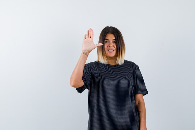 Jovencita mostrando la palma de la mano para saludar con vestido de polo y mirando confiada. vista frontal.