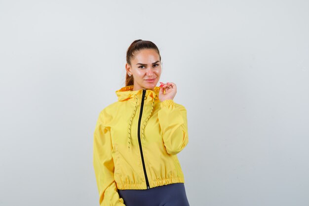 Jovencita posando en chaqueta amarilla y luciendo atractiva, vista frontal.