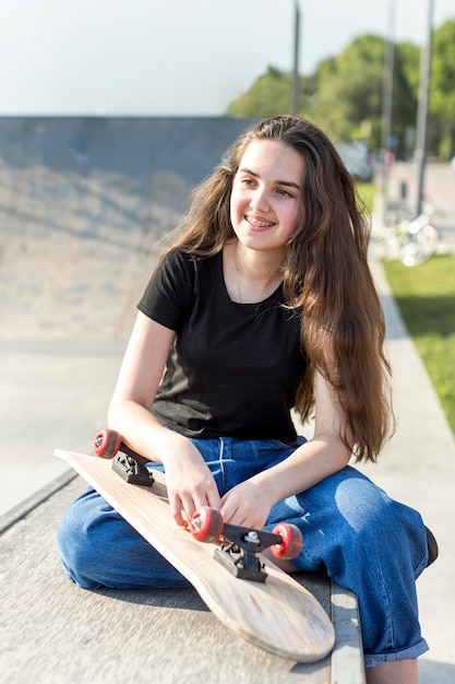 Jovencita posando junto a patineta al aire libre