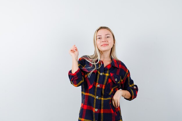 Jovencita posando mientras está de pie en camisa a cuadros y luciendo atractiva, vista frontal.