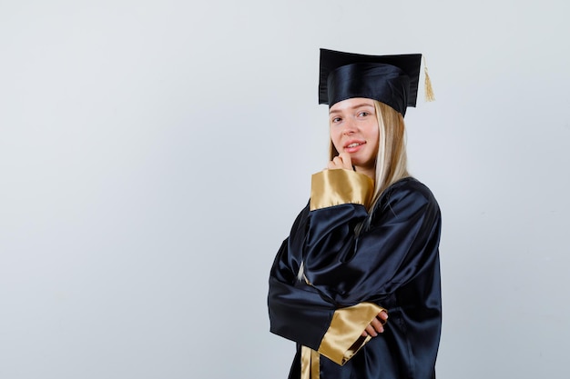 Jovencita posando mientras está de pie en traje académico y se ve atractiva.