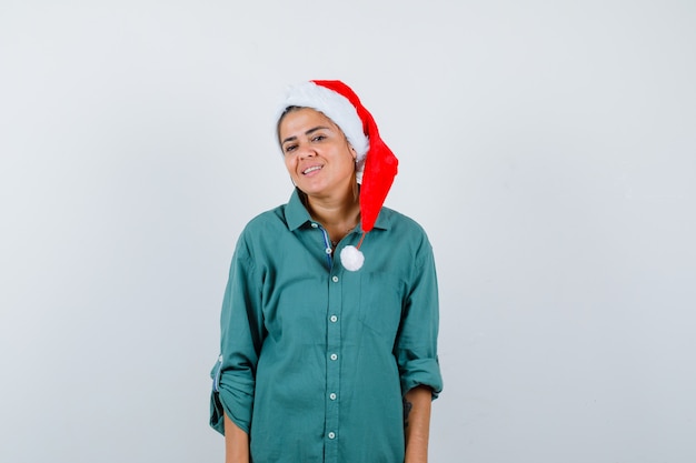 Jovencita posando con sombrero de navidad, camisa y mirando alegre, vista frontal.