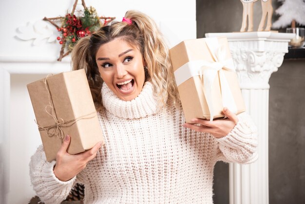 Jovencita rubia con regalos felizmente cerca de la chimenea.