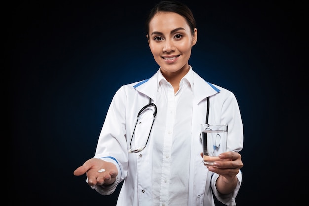 Jovencita sonriendo y sosteniendo píldora y vaso de agua aislado