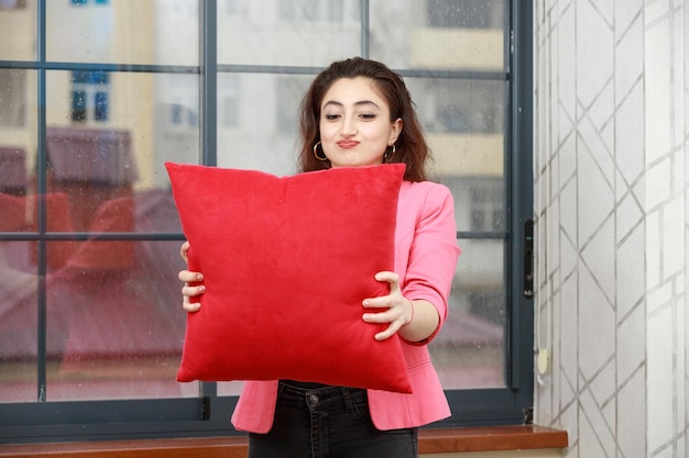 Jovencita sosteniendo una almohada roja y mirándola