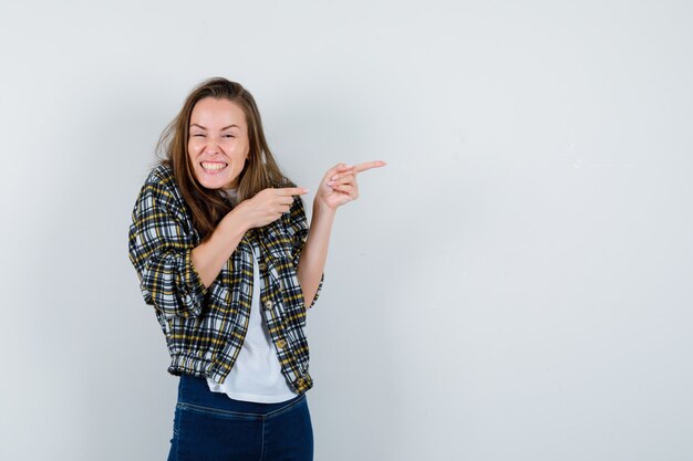 Jovencita sosteniendo las manos juntas en el pecho en camiseta, chaqueta, jeans y mirando feliz, vista frontal.