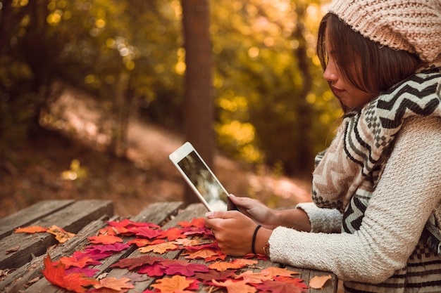 Jovencita con tableta en la mesa en el parque de otoño