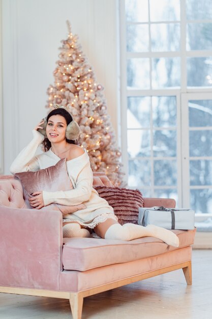 Jovencita vestida de blanco en el sofá en Navidad