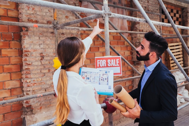 Jóvenes agentes inmobiliarios con andamio de fondo