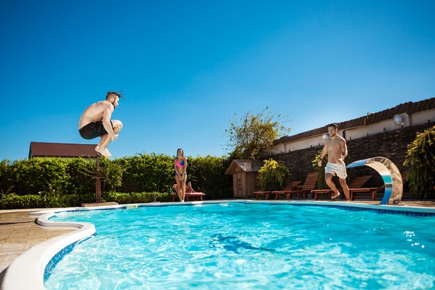 Jóvenes alegres amigos sonriendo, relajándose, saltando en la piscina