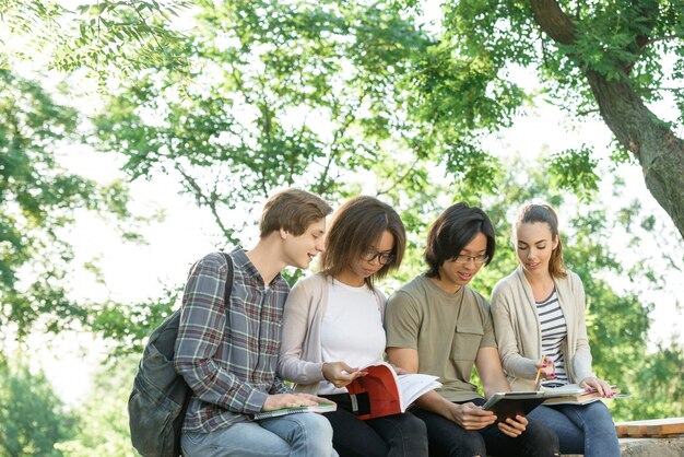 Jóvenes alegres estudiantes sentados y estudiando al aire libre