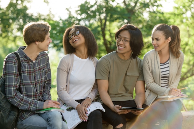 Jóvenes alegres estudiantes sentados y estudiando al aire libre