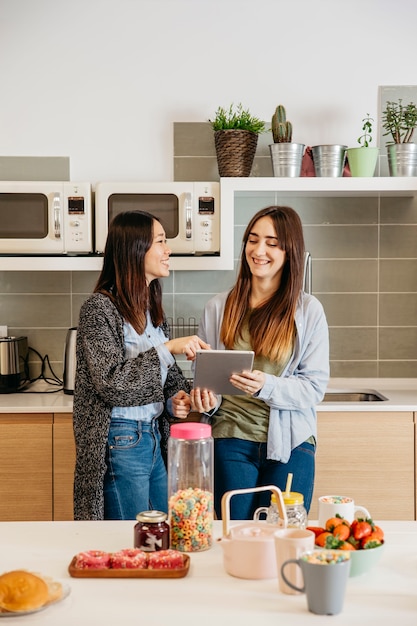 Jóvenes alegres mujeres con tableta en la cocina