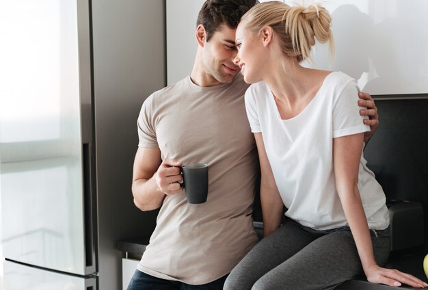 Jóvenes amantes disfrutando de abrazos mientras está de pie en la cocina