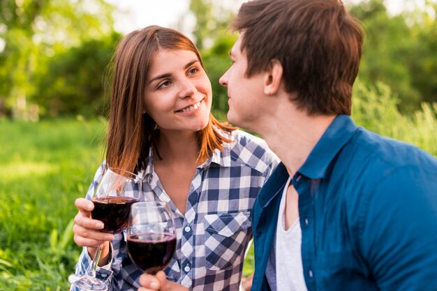 Jóvenes amantes sonrientes tintineando copas de vino afuera