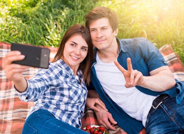 Jóvenes amantes tumbados en manta y tomando selfie