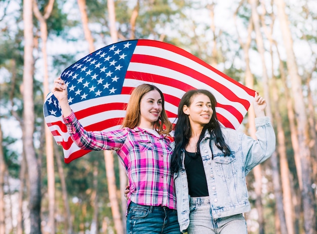 Jóvenes amigas abrazando y agitando la bandera estadounidense