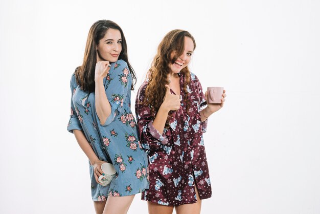 Jóvenes amigas con taza de café gesticular pulgares arriba