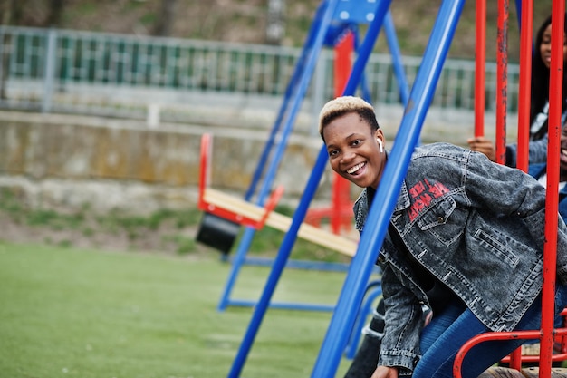 Jóvenes amigos africanos de la generación del milenio en el tobogán y el columpio del patio de juegos Gente negra feliz divirtiéndose juntos Concepto de amistad de la Generación Z