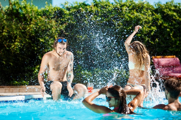 Jóvenes amigos alegres sonriendo, riendo, relajándose, nadando en la piscina