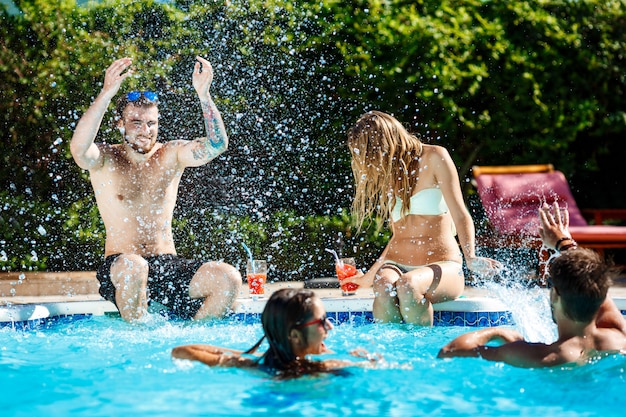Jóvenes amigos alegres sonriendo, riendo, relajándose, nadando en la piscina