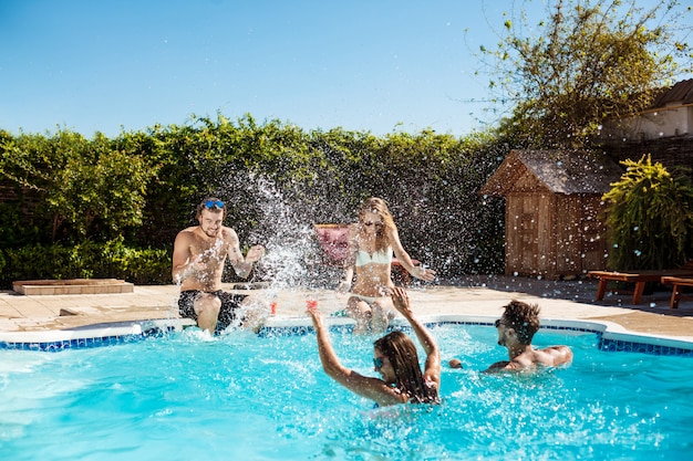 Jóvenes amigos alegres sonriendo, riendo, relajándose, nadando en la piscina