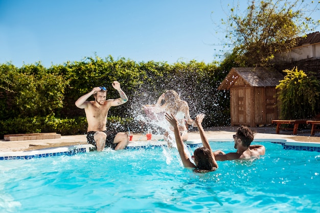 Jóvenes amigos alegres sonriendo, riendo, relajándose, nadando en la piscina