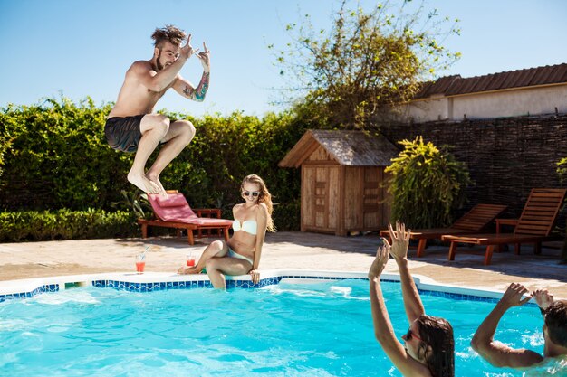 Jóvenes amigos alegres sonriendo, riendo, relajándose, nadando en la piscina