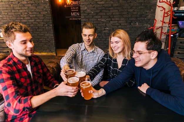 Jóvenes amigos brindando y tintineando con vasos de cerveza en el bar