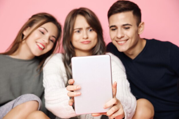 Jóvenes amigos haciendo selfie en tableta en rosa