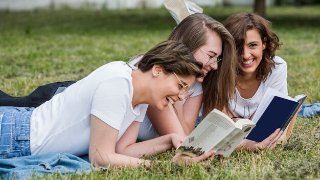 Jóvenes amigos leyendo tumbado en el césped del parque
